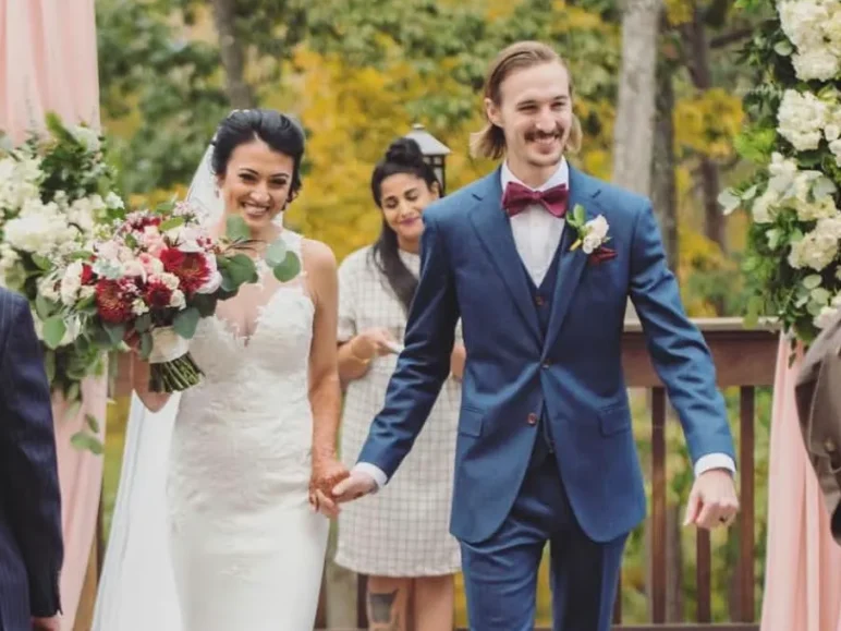 Newlyweds joyfully walking down the aisle under a floral archway crafted by an Atlanta wedding florist, surrounded by guests and autumn foliage.