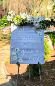 A wedding welcome sign adorned with white daisies and greenery.