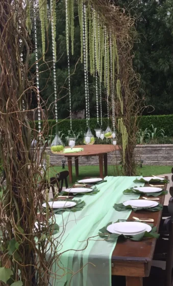An elegantly set outdoor dining table under a natural canopy decorated with Flowers for Weddings, featuring hanging crystal strands and rustic vines.