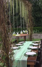 Outdoor wedding reception table with green table runner and hanging decorations.