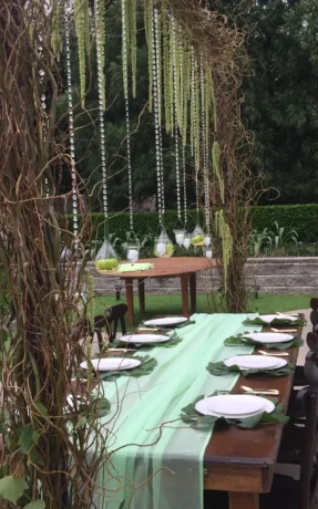 Outdoor wedding reception table with green table runner and hanging decorations.