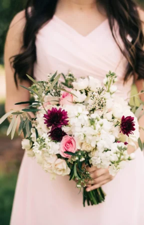 bouquet featuring white hydrangeas, pink roses, dark purple dahlias, and green foliage.