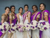 A bride and her bridesmaids at an Indian wedding, all dressed in traditional attire and holding beautifully coordinated bouquets with white and purple flowers.