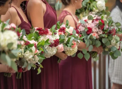 Bridesmaids holding bouquets with chrysanthemums, roses, and greenery in burgundy dresses.