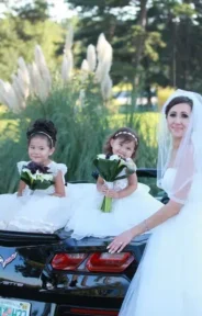 A bride and groom posing with two flower girls on a black car.