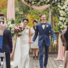 Newlyweds joyfully walking down the aisle under a floral archway crafted by an Atlanta wedding florist, surrounded by guests and autumn foliage.
