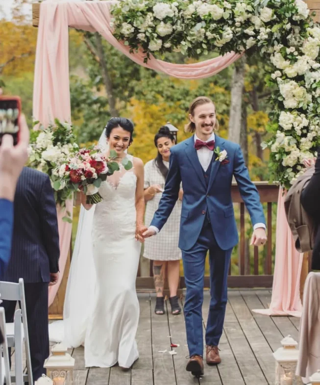 Newlyweds joyfully walking down the aisle under a floral archway crafted by an Atlanta wedding florist, surrounded by guests and autumn foliage.